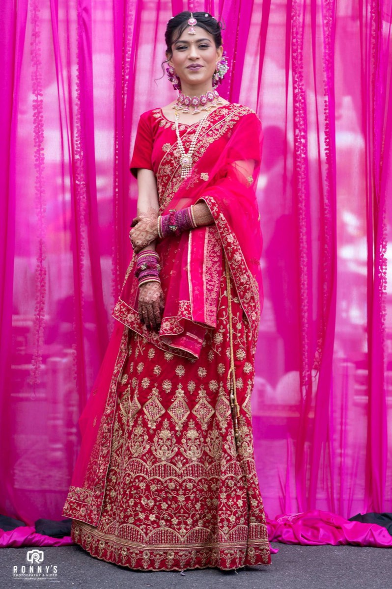 A bride in a red and gold outfit standing in front of bright pink drapes
